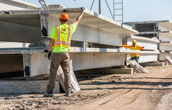 two workers guiding a double tee onto a stack in a shipping yard